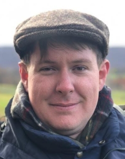 A close-up of a person wearing a hat outside, smiling.